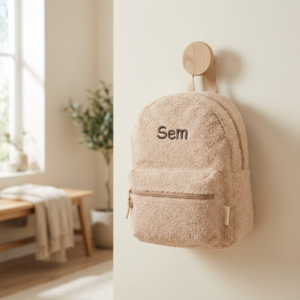 Beige teddy rugzak met naam 'Sem' hangend aan houten wandhaak in lichte kinderkamer